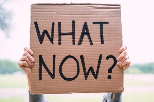 person holding a cardboard banner with what now written on it