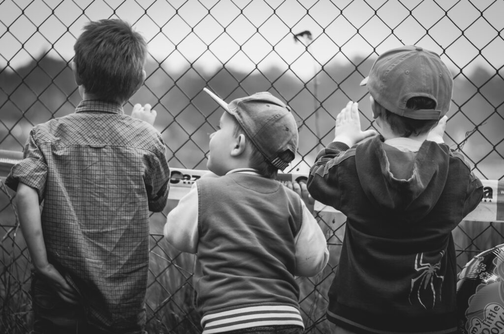 boys watching a baseball game through a fence