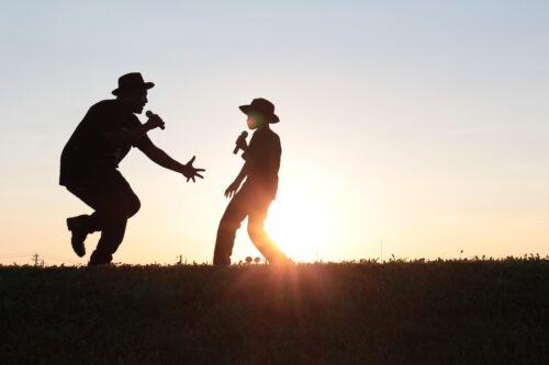 father and son singing in a field wearing cowboy hats during sunset